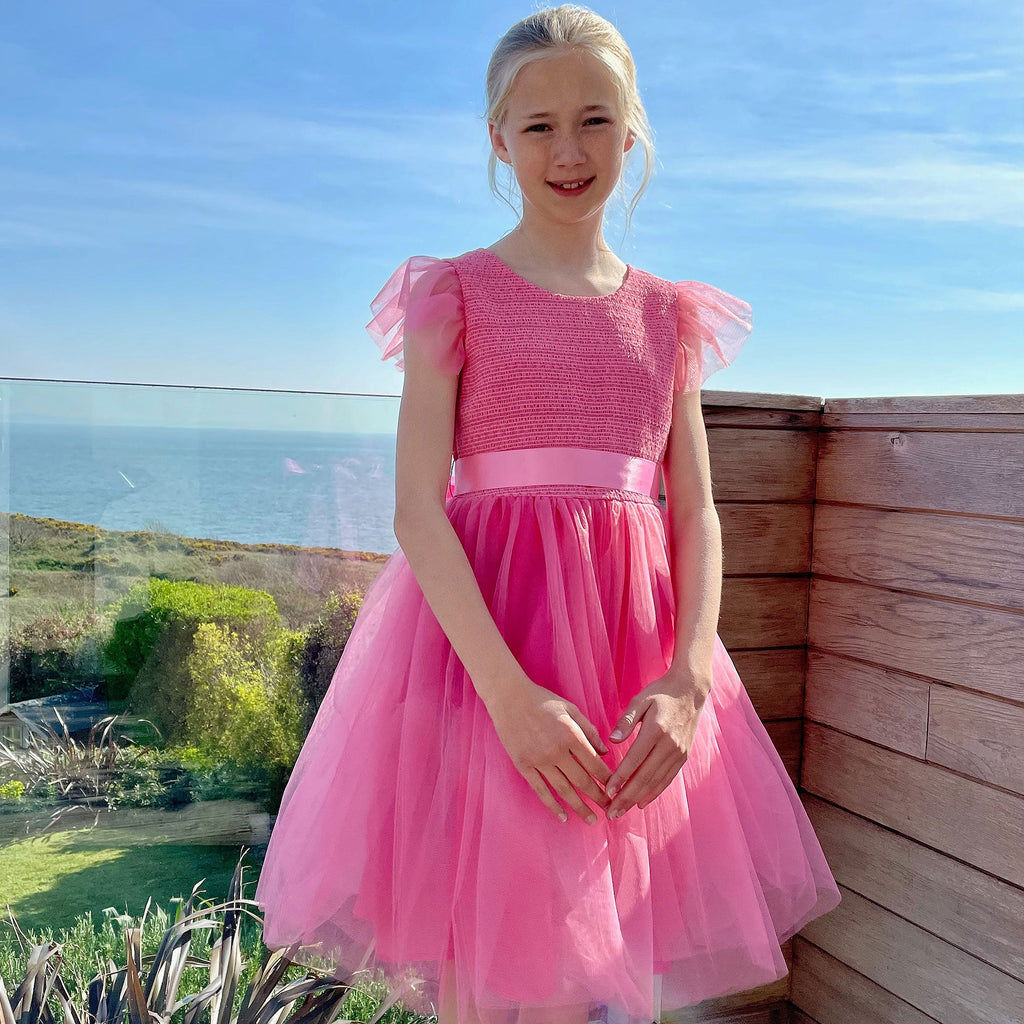 Girl Wearing the Confetti Candy Pink Embroided Smocked  with Tulle by the Garden.